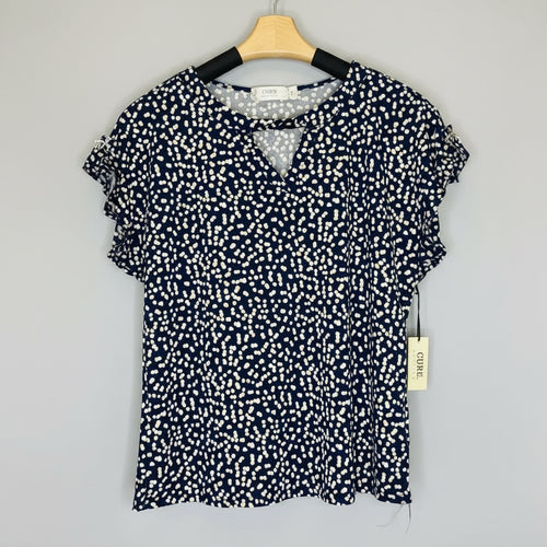Navy blue blouse with white pattern on a hanger against a wooden background