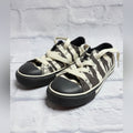 A pair of low-top canvas sneakers with a black and off-white camouflage pattern, cream-colored laces, and black rubber toe caps, resting on a shoebox.