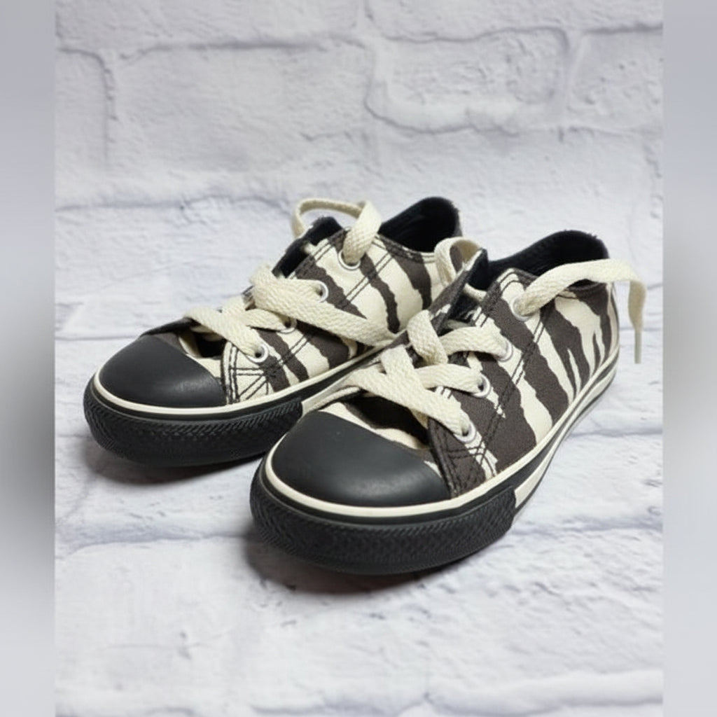 A pair of low-top canvas sneakers with a black and off-white camouflage pattern, cream-colored laces, and black rubber toe caps, resting on a shoebox.