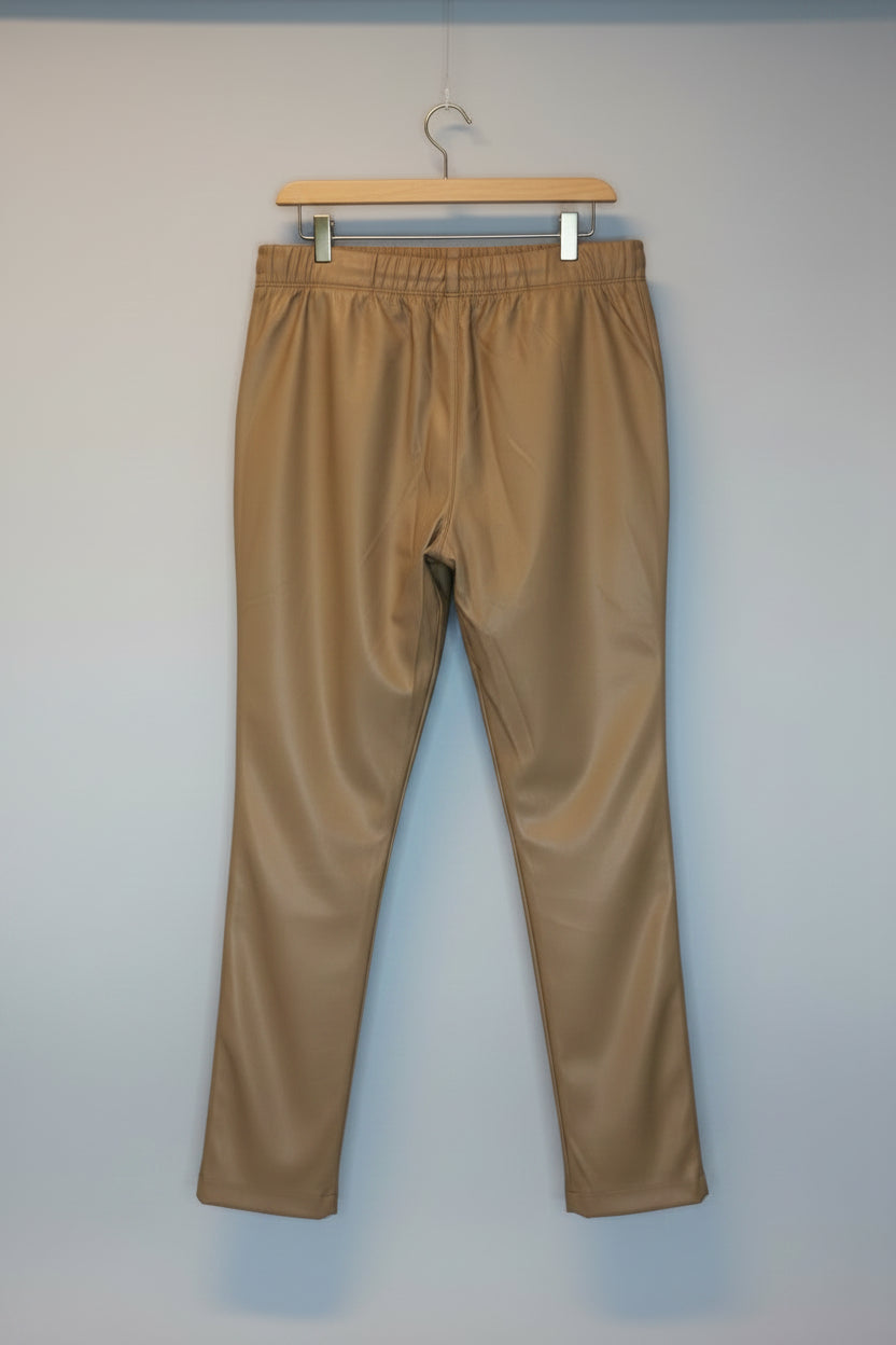 A pair of tan elastic-waist pants hanging against a white brick wall background.
