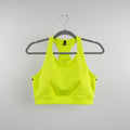 A bright neon yellow athletic sports bra with a scoop neck, hanging on a gray hanger against a light wood background.